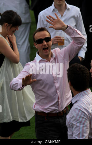 Racegoers genießen einen Drink, während die Saw Doctors während eines Konzerts am Ende des Gold Cup Meetings im Sandown Park auftreten. Stockfoto