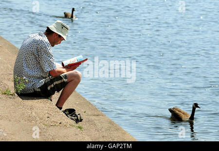 Ein Mann genießt das warme Wetter, als er am Ufer des Trent in der Nähe der Trent Bridge in Nottingham liest. Stockfoto