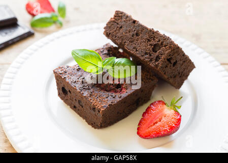 Nahaufnahme von Schokoladen-Brownie Kuchen mit Erdbeeren garniert und arrangiert auf weißen Teller. Selektiven Fokus Stockfoto