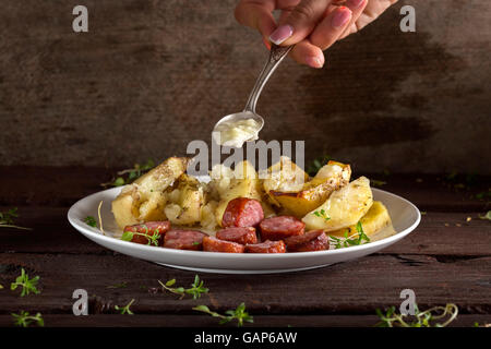 Hand, Knoblauch-Sauce über Bratkartoffeln mit Würstchen und Gewürzen über hölzerne Hintergrund Stockfoto