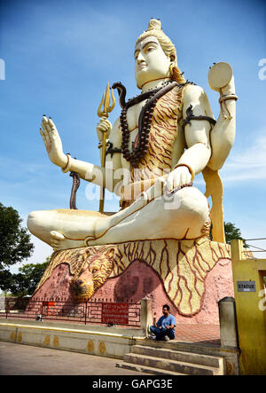 Ein Mann sitzt am Boden des riesigen Lord Shiva-Statue, die segnet Willkommen alle Pilger besuchen Nageshwar Tempel in Gujarat. Stockfoto