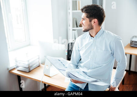 Glückliche junge Geschäftsmann hält Ordner mit Dokumenten und lächelnd in Büro Stockfoto