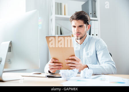 Schön konzentriert junger Geschäftsmann Mann sitzen und Lesen von Notizen im Notizbuch am Arbeitsplatz Stockfoto