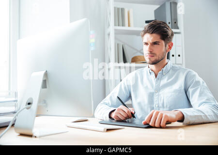 Konzentrierte sich junge Designer arbeiten mit Computer und Grafiktablett am Arbeitsplatz Stockfoto