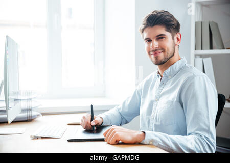 Glücklich Jüngling Designer sitzen und mit Grafiktablett am Arbeitsplatz Stockfoto