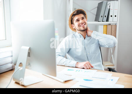 Glücklich entspannt junger Geschäftsmann in Hut sitzen und träumen am Arbeitsplatz Stockfoto