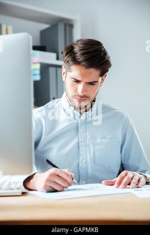 Zuversichtlich Jungunternehmer am Tisch sitzen und unterschreiben im Büro Stockfoto