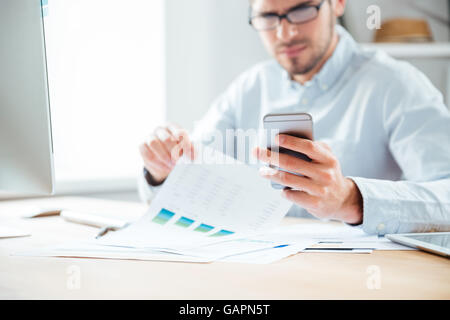 Bild eines glücklichen jungen Geschäftsmann mit Handy während der Arbeit im Büro beschnitten Stockfoto