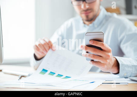 Bild eines nachdenklichen jungen Geschäftsmann mit Handy während der Arbeit im Büro beschnitten Stockfoto