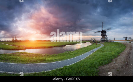 Landschaft mit traditionellen holländischen Windmühlen und Pfad in der Nähe der Wasserkanäle. Wolken am farbenprächtigen Sonnenuntergang im Frühling. Kinderdijk, Neth Stockfoto