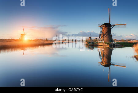 Schöne traditionelle holländische Windmühlen in der Nähe der Wasserkanäle mit Spiegelung im Wasser bei farbenfrohen Sonnenaufgang in berühmte Kinderdijk, Stockfoto