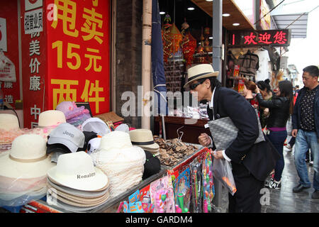 Ein chinesischer Mann versucht eine neue Mütze will er in einem Hut-Geschäft kaufen. Qibao Old Street, Beijing, China. 26.04.2016 Stockfoto