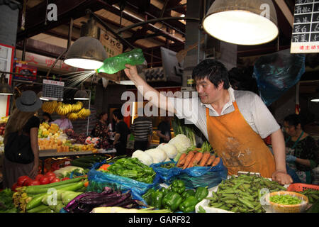 Ein Mann sprüht Wasser auf die Produkte in den bunten Obst und Gemüse Markt im Bereich Tianzifang, das ehemalige französische Viertel. Stockfoto