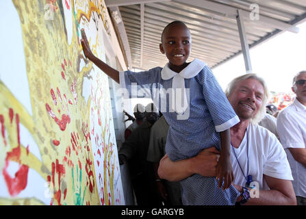 Sir Richard Branson holt ein junges Schulmädchen ab, damit sie von Hand eine Wand eines neuen Gebäudes der Masi Mara Schule in Kenia malen kann. Stockfoto