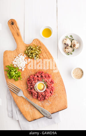 Rindertatar mit gehackten Zwiebeln und Gurken auf Holzbrett serviert Stockfoto