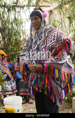 Native peruanischen Mann trägt eine handgewebte Ponchos und eine Chollo - Mütze mit Ohrenklappen, Teilnahme an seine Tochter Hochzeitszeremonie. Neben ihm ist ein Eimer mit Chicha - Bier aus Mais abgeleitet. Stockfoto