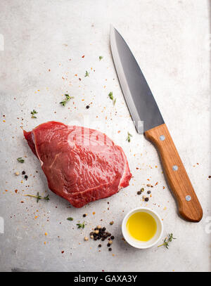 Stück rohes Rindfleisch mit Olivenöl, schwarzem Pfeffer und einem Messer in der Nähe Stockfoto