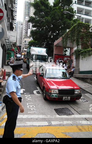 Ein chinesischer Polizist Regie Verkehrs gestikulieren Autos zu stoppen und warten an der Kreuzung... Hong Kong, Hong Kong. 06.05.2016. Stockfoto