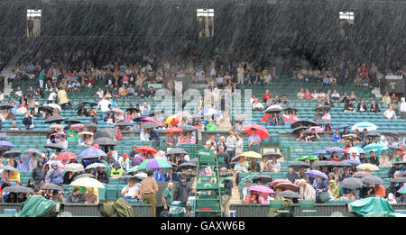 Fans sitzen im Regen auf dem Center Court, da das Spiel während der Wimbledon Championships 2008 im All England Tennis Club in Wimbledon verzögert wird. Stockfoto