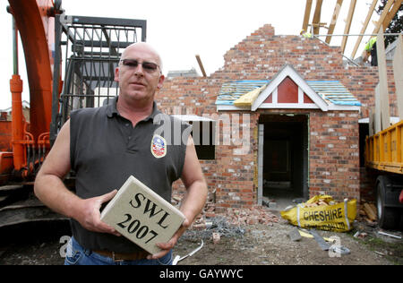 Stephen Woodfinden-Lewis hält den Datumsstein aus seinem Haus, als Abbrucharbeiter das 600,000 neu erbauten Gebäude in Woodford, Cheshire, niederschlagen, nachdem ratsplaner entschieden hatten, dass es zwei Fuß zu groß war. Stockfoto