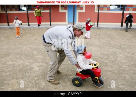 Prinz Harry schiebt die vierjährige Mojabeng auf ihren Traktor während eines Besuchs in der Lesotho Kinderberatung in Maseru, Lesotho, Afrika. Stockfoto