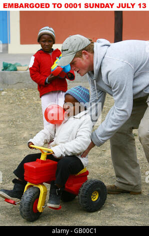 Prinz Harry schiebt die vierjährige Mojabeng auf ihren Traktor während eines Besuchs in der Lesotho Kinderberatung in Maseru, Lesotho, Afrika. Die Lesotho Child Counselling Unit (LCCU) wurde 2002 gegründet, um misshandelten Kindern ein sicheres Haus zu bieten. Stockfoto