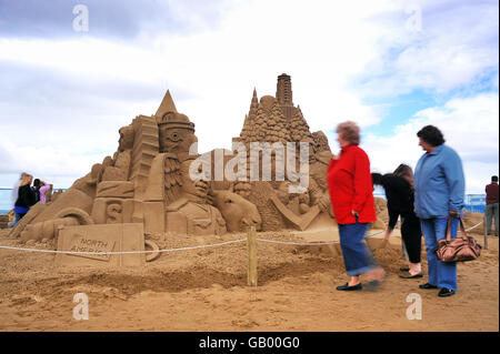 Die Zuschauer kommen an einer nordamerikanischen Sandskulptur vorbei, die aus Totempfählen, Bären, einem Hockeyspieler, Tannen und Gebäuden besteht, die von Jill und Thomas aus Florida am Weston-Super-Mare Beach geformt wurden. Stockfoto