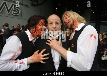 Regisseur George Clarke wird bei der Premiere von Nordirlands erstem Zombie-Horrorfilm „The Battle of the Bone“ in der Odyssey Arena in Belfast von den Zombies Claire Douglas und Johnny Burmside angegriffen. Stockfoto