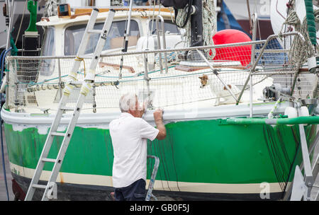 Älterer Mann Reparatur Yacht während Hund ihn vom Deck in Werft in Las Palmas auf Gran Canaria, Kanarische Inseln, Spanien beobachtet Stockfoto