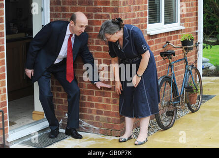 Hochwasserrückgewinnung Minister John Healey hält seine Hand gegen die Wand und zeigt den Wasserstand an, der das Haus von Frau Jane Aston (links) während der Überschwemmungen im letzten Jahr in Tewkesbury überflutete. Stockfoto