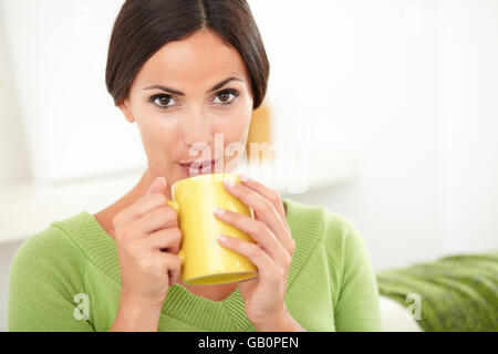 Junge Frau mit braunen Haaren weht auf heißen Kaffee beim Betrachten der Kameras Stockfoto