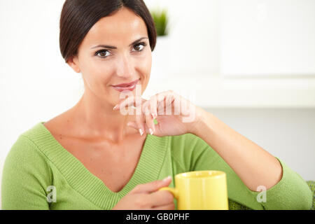 Entspannte Dame mit braunen Haaren einen gelben Becher beim berühren ihr Kinn - Fokus auf Vordergrund halten Stockfoto
