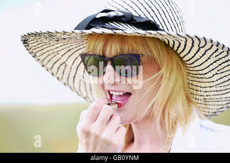 Schöne Frau Auftragen von Lippenstift tragen Diskette Sonne Hut Natur UK Stockfoto