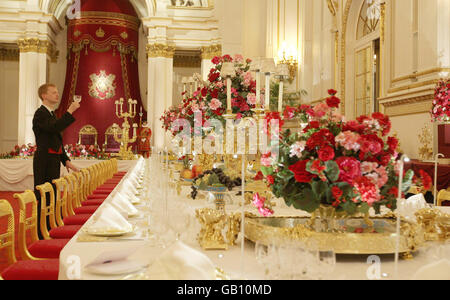 Ein Mitarbeiter inspiziert vor der Sommereröffnung des königlichen Hauses für die Öffentlichkeit einen Weinglas auf dem Festtisch des State Banquet im Ballsaal des Buckingham Palace in London. Stockfoto