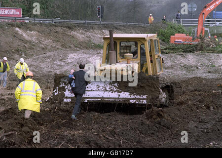 Ein Protestler, der ein kleines Kind trägt, tritt vor eine Planierraupe, saß auf der Wasserwiese in Twyford Down in Hampshire, um die Arbeiten an der M3-Erweiterung zu verhindern. Stockfoto