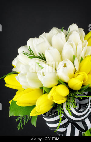 Nahaufnahme von Tulip Bouquet mit gestreiften schwarzen und weißen Band, vor einem dunklen Hintergrund. Stockfoto