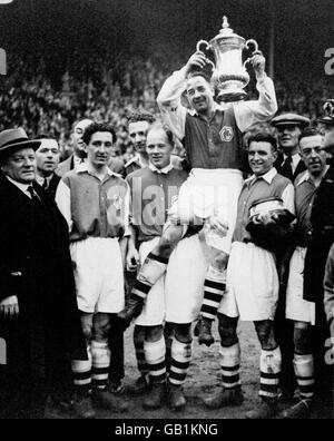 Arsenal-Kapitän Alex James zeigt den FA Cup, als er von seinen siegreichen Teamkollegen gehalten wird: (l-r) Manager George Allison, Ray Bowden, Herbie Roberts, George Male, James, Eddie Hapgood, Joe Hulme Stockfoto