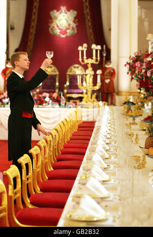 Ein Mitarbeiter inspiziert vor der Sommereröffnung des königlichen Hauses für die Öffentlichkeit einen Weinglas auf dem Festtisch des State Banquet im Ballsaal des Buckingham Palace in London. Stockfoto