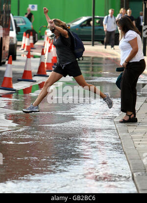 Ein Fußgänger springt auf einer überfluteten Kennington Road außerhalb der Oval-U-Bahnstation im Süden Londons auf einen Wasserpool während eines Wasserlecks. Stockfoto