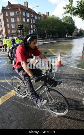 Ein Radfahrer Pedal durch einen Pool von Wasser auf einer überfluteten Kennington Road außerhalb der Oval U-Bahn-Station, Süd-London, während einer Wasserleitung Leck. Stockfoto