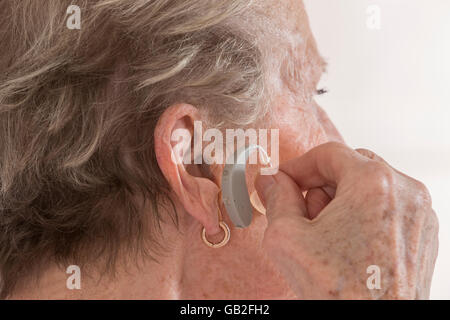 ältere Frau einfügen Hörgerät in ihr hören. Stockfoto