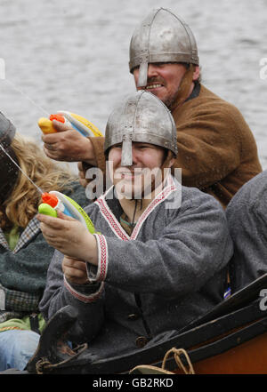 Enthusiasten des National Living History Festival am Lanark Loch in Schottland stellen eine Szene aus der Geschichte wieder auf, als Wikingerstreicher in einem Langschiff an den Küsten Schottlands ankommen - die Wikinger sind mit Wasserpistolen bewaffnet. Stockfoto