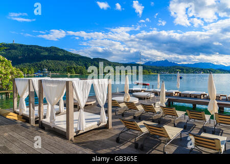 Liegestühle und liegen am Holzdeck und Blick auf den wunderschönen alpinen See Wörthersee im Sommer, Österreich Stockfoto