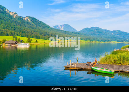 Unbekannter Mann sitzen auf hölzerne Pier und Angeln am Ufer des Weißensee im Sommerlandschaft der Alpen, Österreich Stockfoto