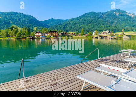 Sonnenliegen auf hölzernen Pier am Ufer des Weißensee in Sommerlandschaft Carinthia Land, Österreich Stockfoto