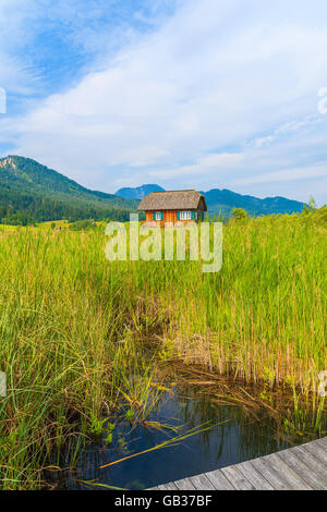 Hölzerne Pier am Ufer des Weißensee und typische alpine House in Ferne im Sommerlandschaft der Alpen, Österreich Stockfoto