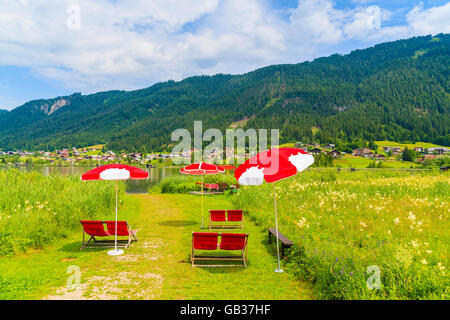 Sonnenschirme mit liegen am Strand am Weißensee im Sommerlandschaft der Alpen, Österreich Stockfoto