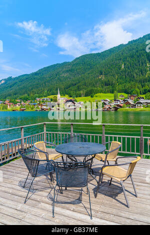 Tisch mit Stühlen auf Holzterrasse und Blick auf grüne Wasser Weißensee im Sommerlandschaft der Alpen, Österreich Stockfoto