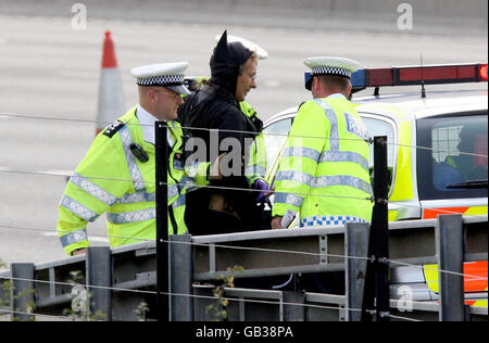 Der als Batman verkleidete Wahlkämpfer Geoffrey Hibbert (Mitte), der vermutlich mit Fathers 4 Justice verbunden ist, wurde von Polizisten begleitet, nachdem er eine Gantry über die M25 nahe dem Flughafen Heathrow in London bestiegen hatte. Stockfoto