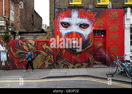 Eine junge Frau geht durch ein Stück der Straßenkunst Dale Grimshaw in Hanbury Street, direkt an der Brick Lane, London. Stockfoto